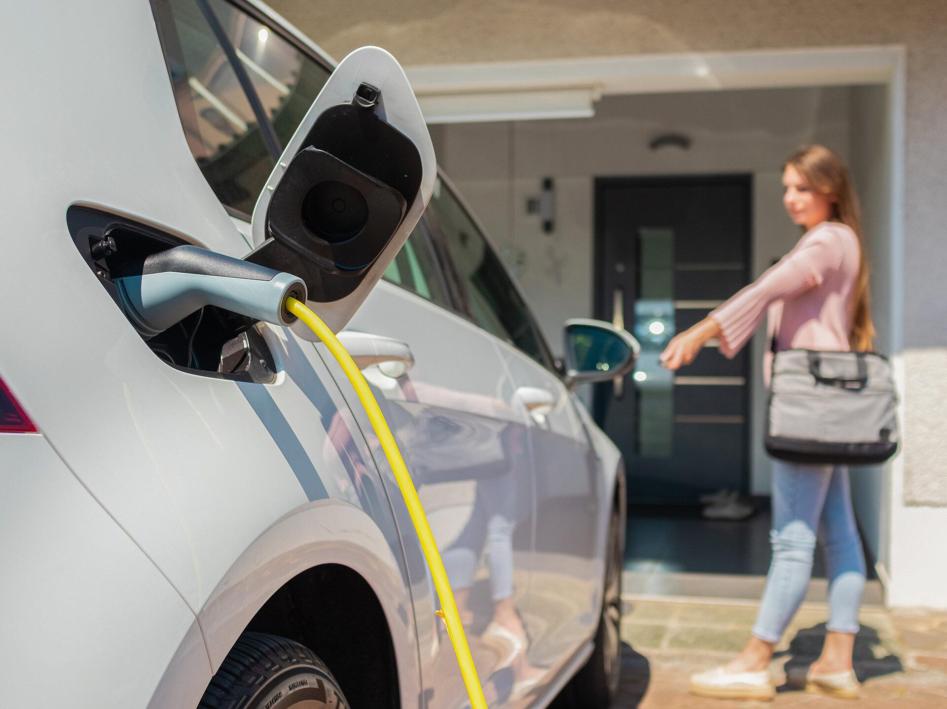 Eine Frau ist zuhause angekommen und hat ihr E-Auto an die Wallbox des Hauses angeschlossen.