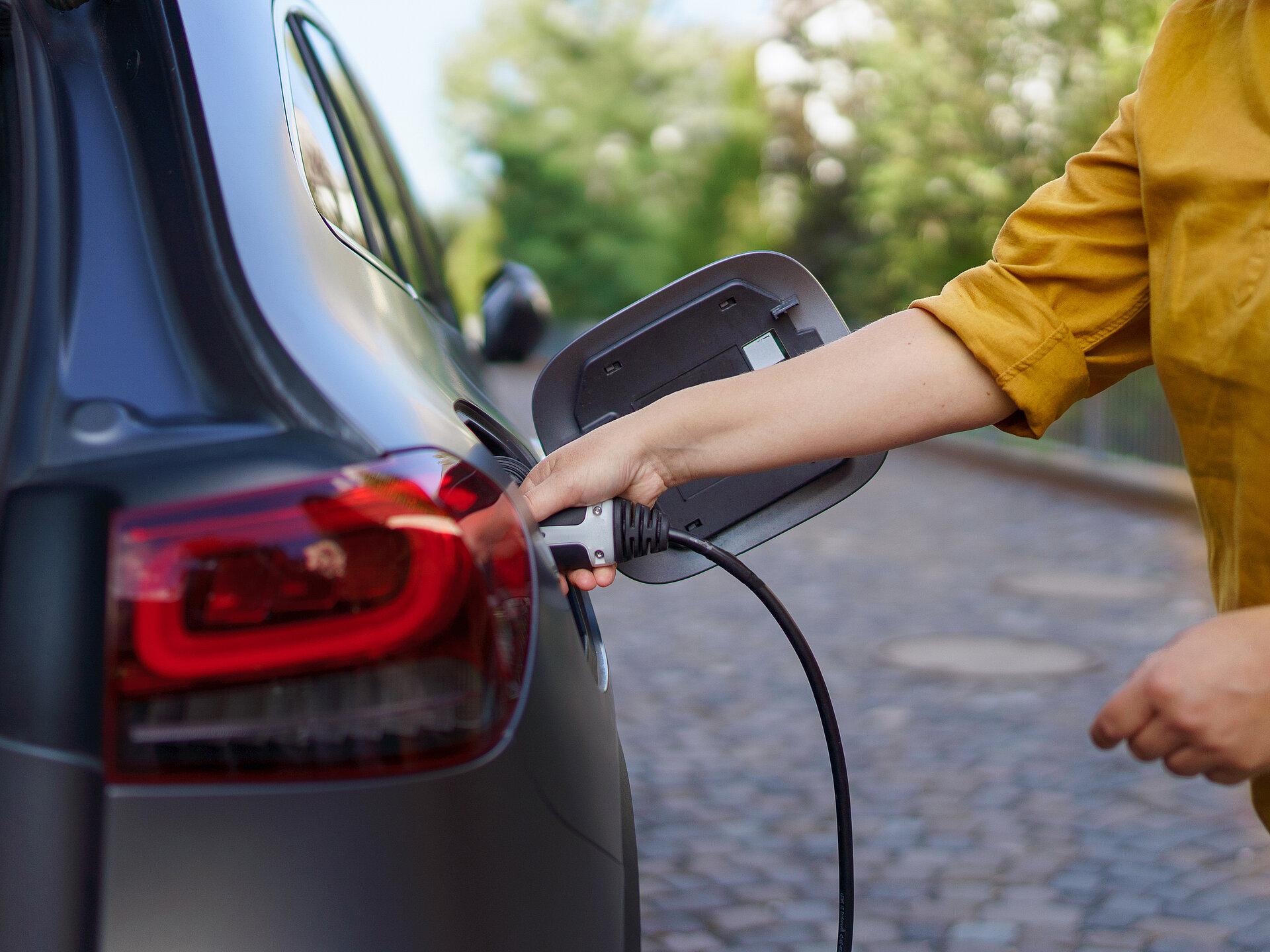 Eine Frau hält den Ladestecker eines E-Autos, das gerade mit Strom geladen wird.