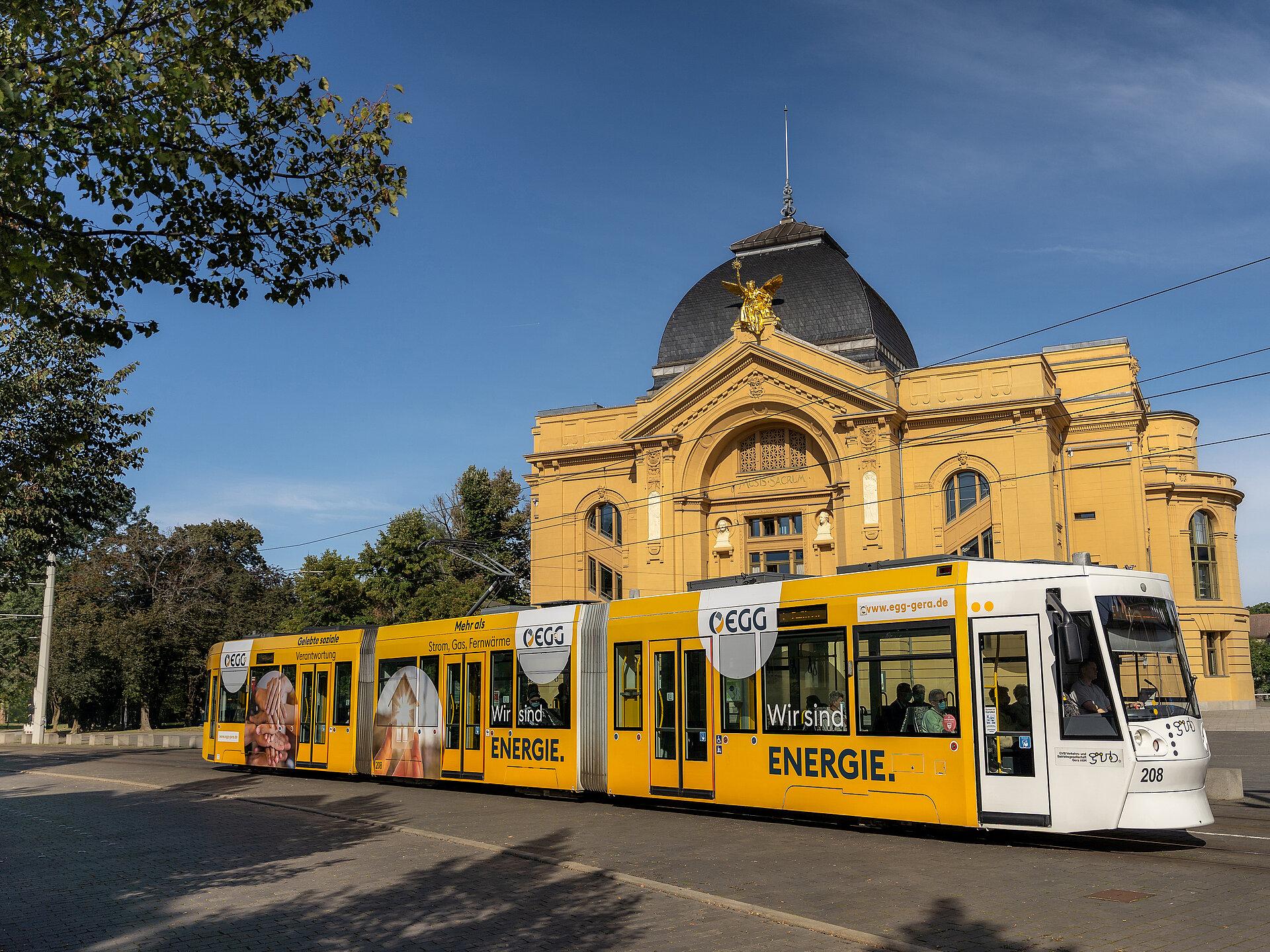 Eine Geraer Straßenbahnen im Design der EGG vor dem Geraer Theater bei Sonnenschein 
