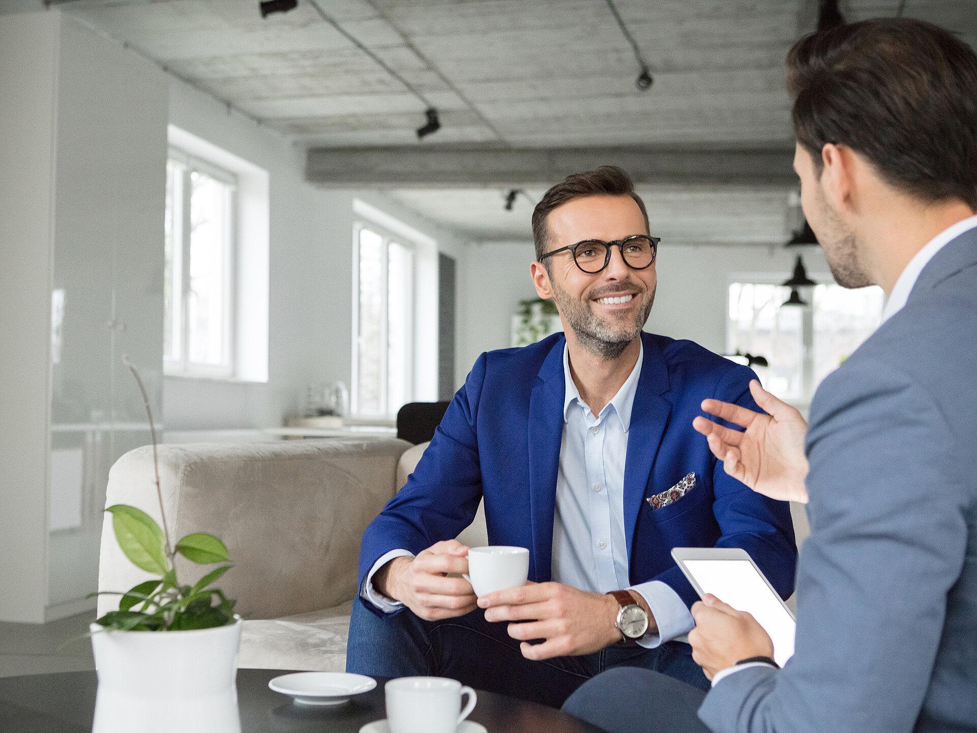 Zwei Geschäftsleute in Anzug führen ein Gespräch bei einer Tasse Kaffee