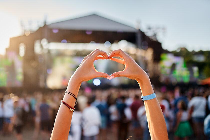 Konzertbesucher formt Herzform mit Händen bei einem Konzert vor einer Bühne im Freien