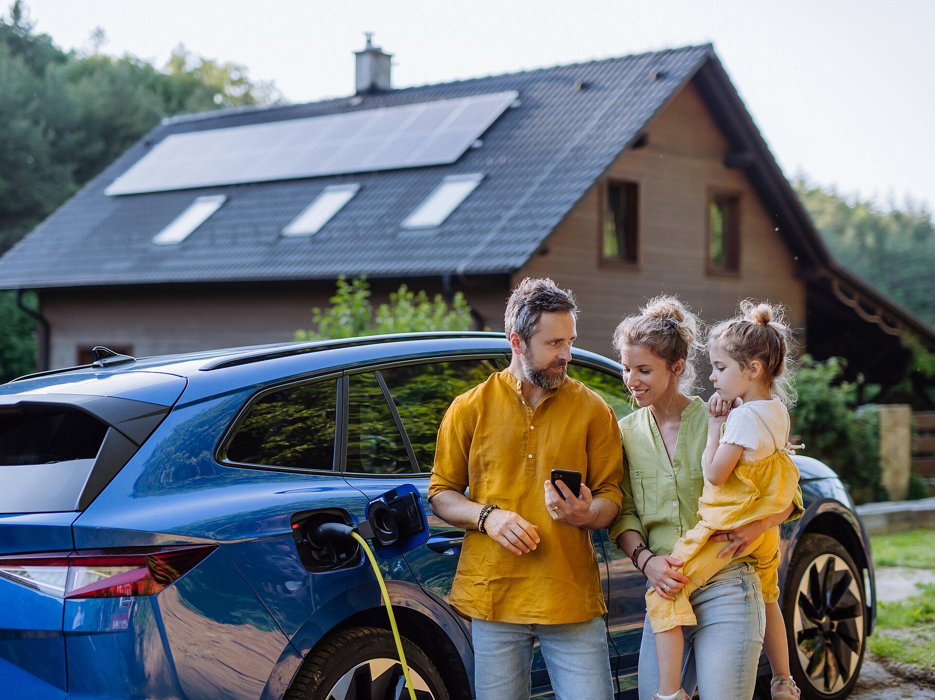 Eine fröhliche Familie lädt ein E-Auto vor einem Haus mit einer PV-Anlage.
