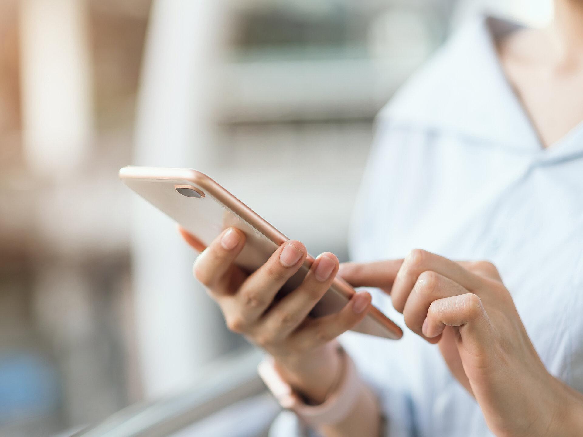 Nahaufnahme einer Frauenhand die ein rosefarbenes Smartphone hält und mit einem Finger darauf tippt