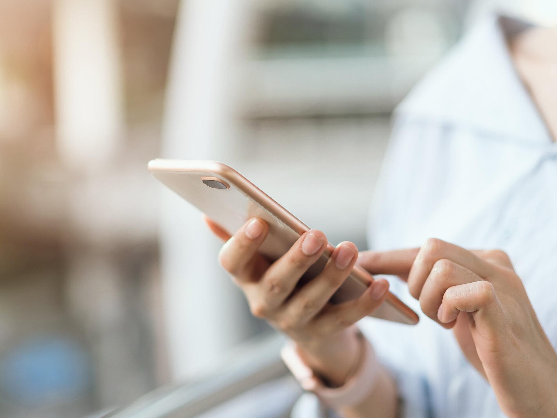 Nahaufnahme einer Frauenhand die ein rosefarbenes Smartphone hält und mit einem Finger darauf tippt
