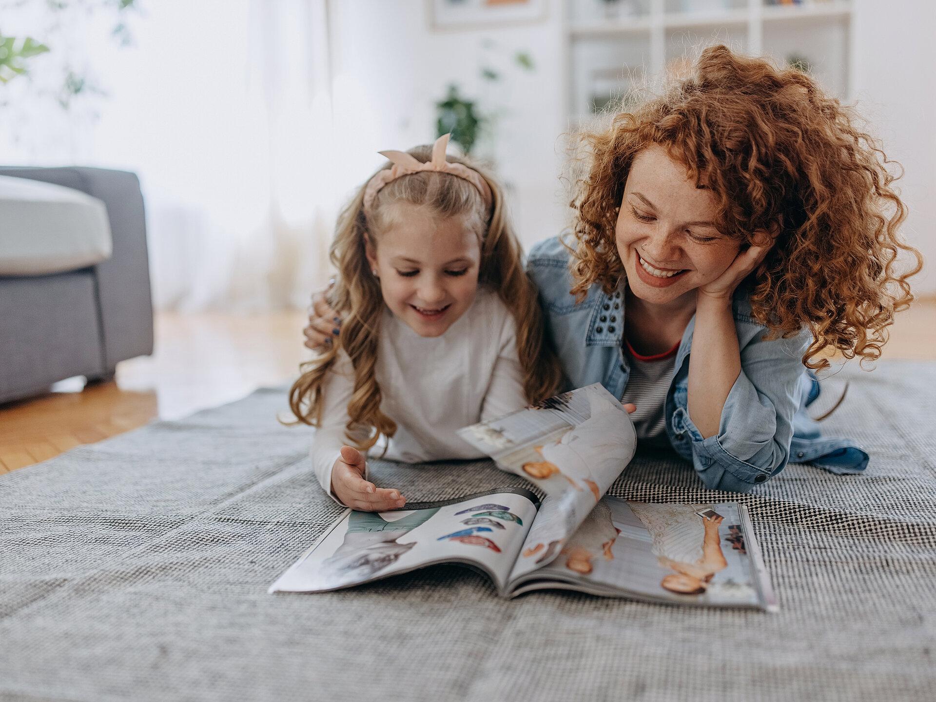 Eine Mutter und eine Tochter liegen auf einem Teppich und blättern in einem Magazin